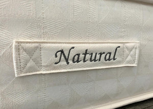 Close-up of The Brick 'Natural' Mattress, showing its textured cream fabric and embroidered "Natural" label.