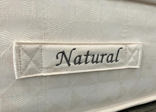 Close-up of The Brick 'Natural' Mattress, showing its textured cream fabric and embroidered "Natural" label.