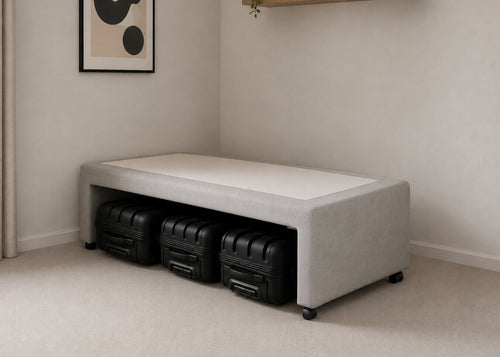 Single grey upholstered divan base with hidden suitcase storage, non-slip top, and black luggage underneath.