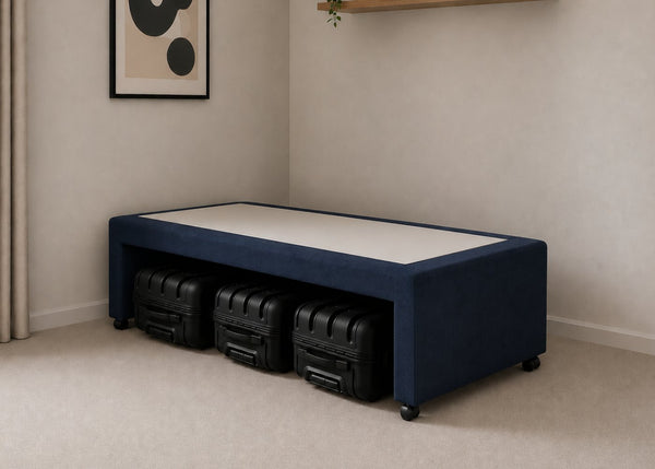 Single navy blue upholstered divan base with hidden suitcase storage, non-slip top, and black luggage underneath.