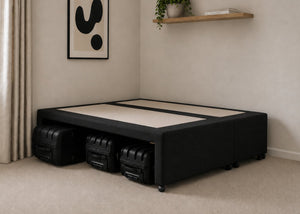 Black upholstered divan base with hidden suitcase storage, non-slip top, and black luggage underneath.