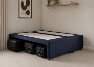 Navy blue upholstered divan base with hidden suitcase storage, non-slip top, and black luggage underneath.