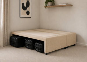 Sand upholstered divan base with hidden suitcase storage, non-slip top, and black luggage underneath.