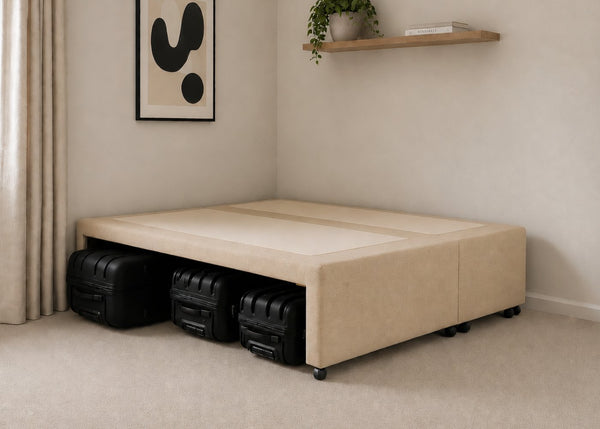 Sand upholstered divan base with hidden suitcase storage, non-slip top, and black luggage underneath.